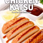 Golden Crispy Chicken Katsu served on a heavy, luxurious square white plate with a matching square sauce dish, drizzled diagonally in a gourmet style with tonkatsu sauce, accompanied by lemon wedges, on a white marble background with fresh herbs and a white towel in the background for FoodForYourGood.com