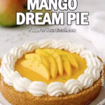 Golden Mango Dream Pie on a white plate, topped with whipped cream, fresh mango slices, and lime zest on a marble countertop with mango and lime in the background.