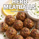 Plate of Greek Herb Meatballs with lemon wedges and creamy yogurt sauce on FoodForYourGood.com