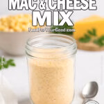 Homemade Mac & Cheese Mix in a glass jar on white marble with cheddar and herbs in background.