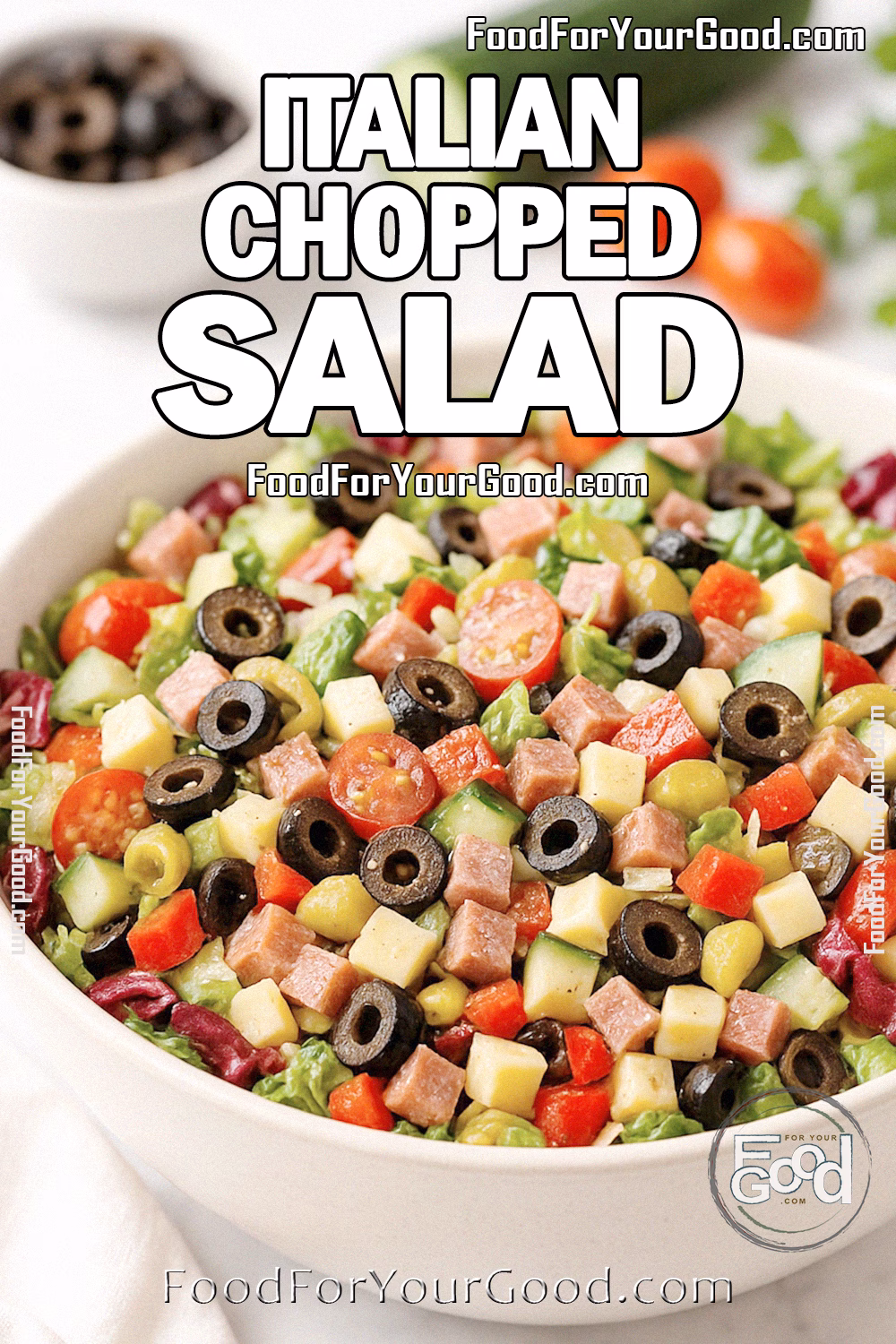 Italian Chopped Salad Recipe | FoodForYourGood.com Italian Chopped Salad in a white bowl with fresh vegetables, salami, cheese, and olives on marble countertop.