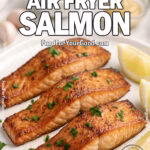 Air Fryer Salmon fillets with lemon wedges and parsley served on a white plate, styled on a marble countertop with fresh ingredients in the background.