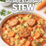 One Pot Sausage & Cabbage Stew in a white ceramic bowl on marble counter, filled with sausage, cabbage, carrots, and tomatoes, with fresh vegetables in background.