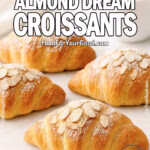 Parisian Almond Dream Croissants on a white marble board, golden and flaky, coated with a generous layer of toasted almond slices and powdered sugar, with a white coffee cup and towel in the blurred background.