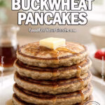 Rustic Buckwheat Pancakes stacked high on a white ceramic plate, topped with melting butter and maple syrup, styled with berries and syrup jar in the background.