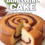 Rustic Jam Swirl Cake on a round white marble board, with one slice cut to reveal golden moist crumb and jam swirls, styled with a bowl of jam, mint leaves, and a white towel in the softly blurred background.