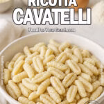 Rustic Ricotta Cavatelli in a white ceramic bowl on a marble countertop, with fresh ricotta, egg, flour, Parmesan, and basil blurred in the background, alongside a folded white towel.