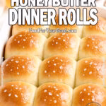 Salted Honey Butter Dinner Rolls in a white baking dish on marble with honey, butter, and flaky sea salt.