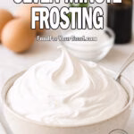 Bowl of homemade Seven-Minute Frosting with glossy peaks, surrounded by eggs, sugar, and vanilla on a white marble counter at FoodForYourGood.com