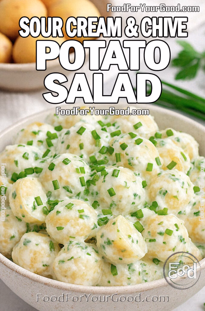 A rustic ceramic bowl filled with sour cream and chive potato salad, garnished with fresh chives, surrounded by whole baby potatoes and herbs on a marble surface.