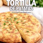 Spanish Tortilla de Patatas served on a white marble surface, garnished with parsley, with potatoes and onion in the background.