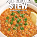Spiced Red Lentil Stew in a white ceramic bowl with red lentils, crushed tomatoes, and onions, garnished with cilantro and a lemon wedge.