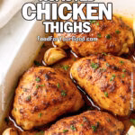 Spicy Honey Roasted Chicken Thighs with crispy golden skin in a white baking dish, garnished with garlic and lemon wedges.