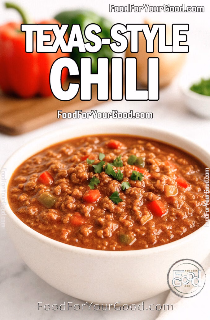 Texas-Style Chili in a white ceramic bowl on a white marble countertop, garnished with fresh cilantro and surrounded by bell peppers, onion, and herbs in the background.