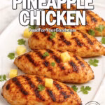 Tropical Pineapple Chicken on FoodForYourGood.com – grilled pineapple-marinated chicken breasts on an upscale white pointed-corner platter with pineapple chunks and cilantro, white towel, and herbs on a marble background.