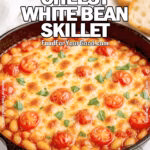 Tuscan Cheesy White Bean Skillet in a cast iron pan with golden melted cheese, cherry tomatoes, and basil, served with crusty bread on a marble countertop.