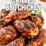 Ultimate Grilled BBQ Chicken on FoodForYourGood.com, featuring charred and juicy BBQ-glazed chicken drumsticks and thighs stacked on a white plate, garnished with parsley on a marble background.