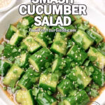 Asian Smash Cucumber Salad in a white ceramic bowl, dressed with soy-sesame sauce, garnished with sesame seeds, cilantro, and scallions on a marble surface.