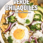 Best Verde Chilaquiles served in a rustic white dish on marble, topped with sunny-side-up eggs, salsa verde, avocado, queso fresco, red onion, jalapeños, and cilantro.