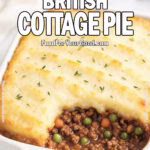 Classic British Cottage Pie baked in a white ceramic dish with rustic mashed potato topping, golden at the edges. A portion is scooped out, revealing savory beef, peas, and carrots filling beneath.