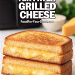 Crispy Air Fryer Grilled Cheese with golden sourdough bread and melted cheddar layered inside, styled on white marble with air fryer in background.