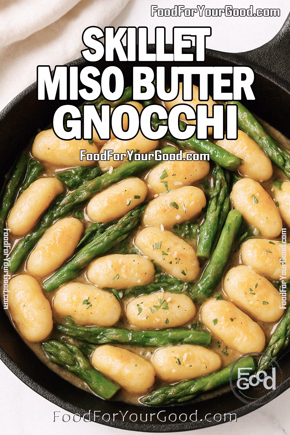Skillet Miso Butter Gnocchi Recipe - FoodForYourGood.com Skillet Miso Butter Gnocchi with thin asparagus in a round black cast iron skillet on a white marble countertop. The skillet is filled with golden gnocchi coated in glossy miso butter sauce, with a soft white towel and fresh herbs in the blurred background.