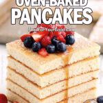Fluffy Oven-Baked Pancakes stacked into golden squares on a white luxurious plate, drizzled with maple syrup and topped with fresh berries. A sheet pan of pancakes rests blurred in the background on FoodForYourGood.com