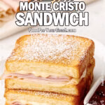Golden French Monte Cristo Sandwich on a square white plate with ham, turkey, and melted cheese, served with raspberry preserves on FoodForYourGood.com