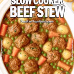 Rustic Slow Cooker Beef Stew in a white slow cooker filled with tender beef chunks, golden potatoes, carrots, peas, and celery in a rich brown broth, on a white marble countertop with fresh herbs and vegetables around.
