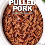 Slow Cooker BBQ Pulled Pork in a white slow cooker, tender shredded meat drizzled with barbecue sauce, styled on a marble countertop with fresh parsley, garlic, and a white towel.