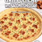 Southern Grits Quiche with Bacon and Cheddar in a white ceramic dish on a marble countertop, garnished with fresh chives, crispy bacon, and herbs in the background.