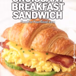 Sunrise Croissant Breakfast Sandwich on a square white plate with scrambled eggs, melted cheddar, avocado, and bacon.