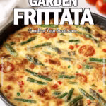 Golden Tuscan Garden Frittata baked in a cast iron skillet with asparagus, cherry tomatoes, red bell pepper, and onion on a white marble countertop.